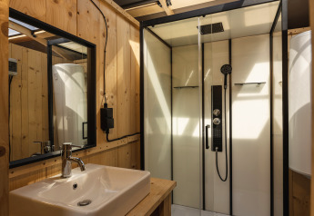 Salle de bain moderne avec parois bois, cabine de douche, lavabo et puits de lumière dans un glamping.