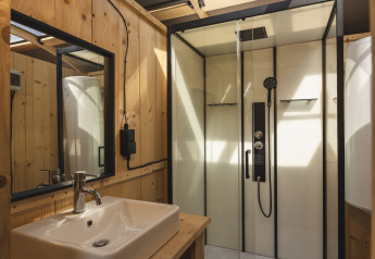 Moderne badkamer met houten wanden, douchecabine, wastafel en dakraam in glamping accommodatie.