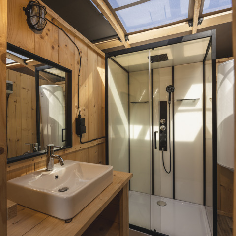 Moderne badeværelse med træpaneler, brusekabine, håndvask og loftsvindue i glamping indkvartering.