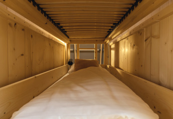 Espace de couchage glamping douillet avec murs en bois, lit confortable et lumière tamisée, vu de l'intérieur.