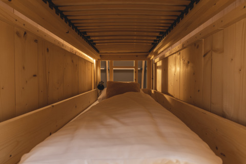 Accogliente area glamping con pareti in legno, letto confortevole e luce soffusa, vista dall’interno.