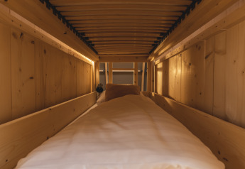 Accogliente area glamping con pareti in legno, letto confortevole e luce soffusa, vista dall’interno.