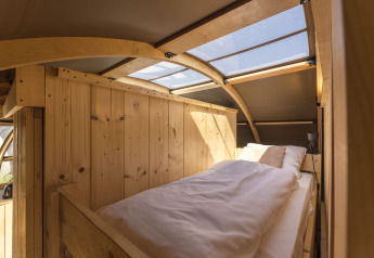 Intérieur de glamping chaleureux avec un lit simple, des murs en bois et une fenêtre de toit.