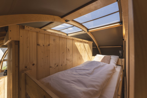 Intérieur de glamping chaleureux avec un lit simple, des murs en bois et une fenêtre de toit.