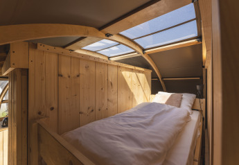 Interior acogedor de glamping con cama individual, paredes de madera y tragaluz en el techo.