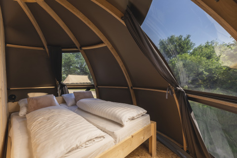 Cozy glamping accommodation with comfortable beds and large windows overlooking green nature.