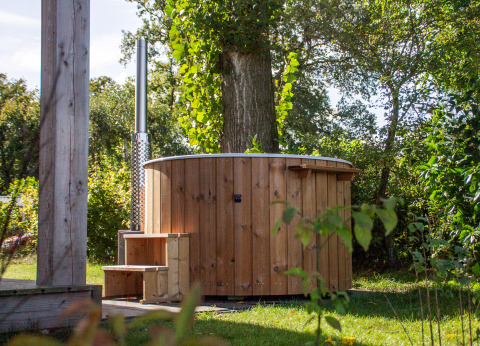 Holz-Whirlpool im Freien neben einer kleinen Hütte im grünen Vakantiepark Hölte in den Niederlanden.