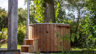 Udendørs træhot tub ved siden af et lille hus i grønne omgivelser i Vakantiepark Hölte, Holland.