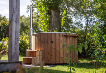 Houten hot tub buiten naast een kleine cabin bij Vakantiepark Hölte in Nederland, omgeven door groen.