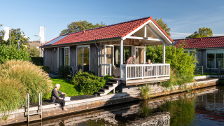 Senioren genießen ihre Zeit an einer Lodge am Wasser mit rotem Dach in Meine, Tusken de Marren, Niederlande.