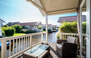 Blick von einer Lodge-Terrasse mit Rattanmöbeln und Glastisch auf einen Kanal mit Ferienhäusern.