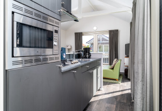 Moderne kitchenette in lodge Meine bij Tusken de Marren, Nederland, met grijze kasten en zithoek.