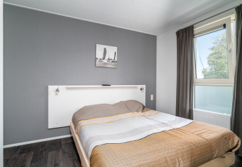 Lichte lodge slaapkamer met een grijze muur, raam, tweepersoonsbed en eenvoudige inrichting.