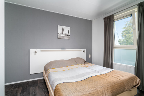 Lichte lodge slaapkamer met grijze accentmuur, raam, tweepersoonsbed en minimalistische inrichting.