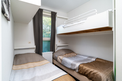 A cozy lodge room featuring two single beds, an overhead bunk, white walls, and a window with curtains.