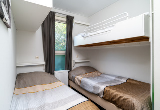 A cozy lodge room featuring two single beds, an overhead bunk, white walls, and a window with curtains.