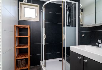 Moderne lodgebadkamer met glazen douchecabine, witte wastafel, houten rek en zwarte tegelwanden.