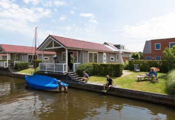 Lodge Meine bij Tusken de Marren in Nederland met gasten, een tuin en een bootje aan het water.