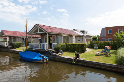Lodge Meine bij Tusken de Marren in Nederland met gasten aan het water en een afgedekte boot aan de steiger.