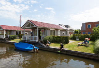 Lodge Meine bij Tusken de Marren in Nederland met gasten aan het water en een afgedekte boot aan de steiger.