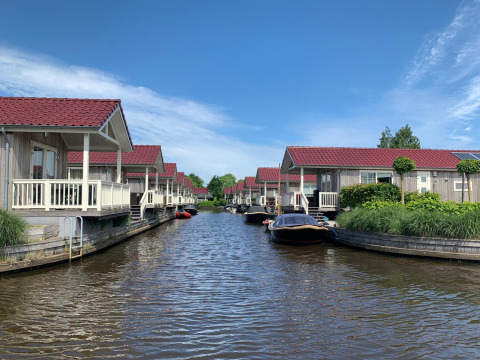 Foto af hytter ved vandet med røde tage, både fortøjet og en blå himmel, taget på en hyggelig lodge.
