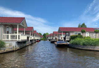 Foto af hytter ved vandet med røde tage, både fortøjet og en blå himmel, taget på en hyggelig lodge.