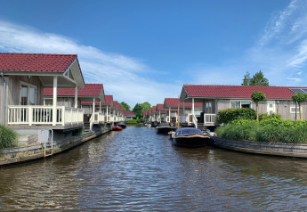 Foto af hytter ved vandet med røde tage, både fortøjet og en blå himmel, taget på en hyggelig lodge.