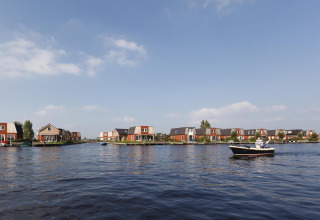 Afbeelding van glampingverblijven aan het water, met een boot op de voorgrond en heldere lucht.
