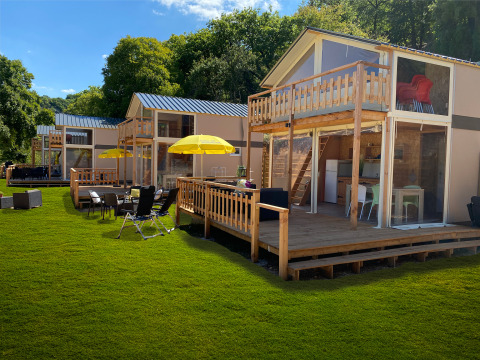 Tente lodge de luxe Belle Vue à La Draille, France, avec terrasses en bois, parasols et pelouse verte.