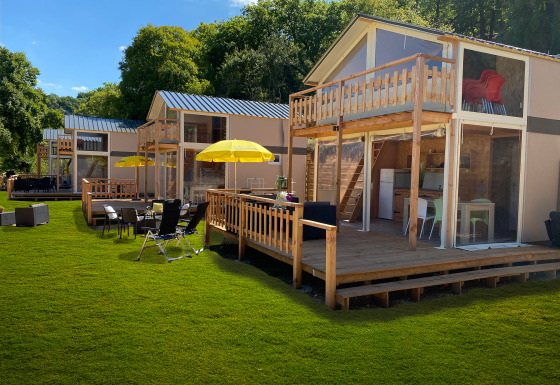 Tente lodge de luxe Belle Vue à La Draille, France, avec terrasses en bois, parasols et pelouse verte.