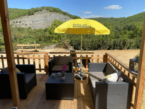 Terraza de madera en la tienda de lujo Belle Vue en La Draille, Francia, con asientos y sombrilla amarilla.