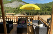 Terraza de madera en la tienda de lujo Belle Vue en La Draille, Francia, con asientos y sombrilla amarilla.