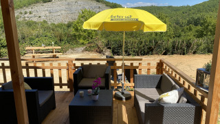 Wooden terrace at luxury lodge tent Belle Vue at La Draille in France, with outdoor seating and a yellow parasol.