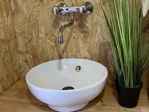 Modern sink with white vessel basin, chrome faucet, and green plant on wood in luxury tent at La Draille.