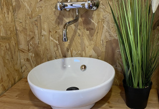 Lavabo moderno con ciotola bianca, rubinetto cromato e pianta verde in tenda safari di lusso a La Draille.
