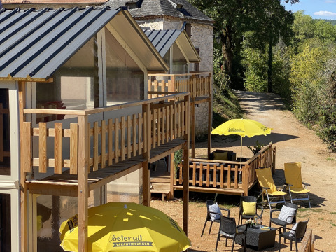 Buitenzone van de luxe lodgetent Belle Vue bij La Draille in Frankrijk met zonnige terrassen en gele stoelen.