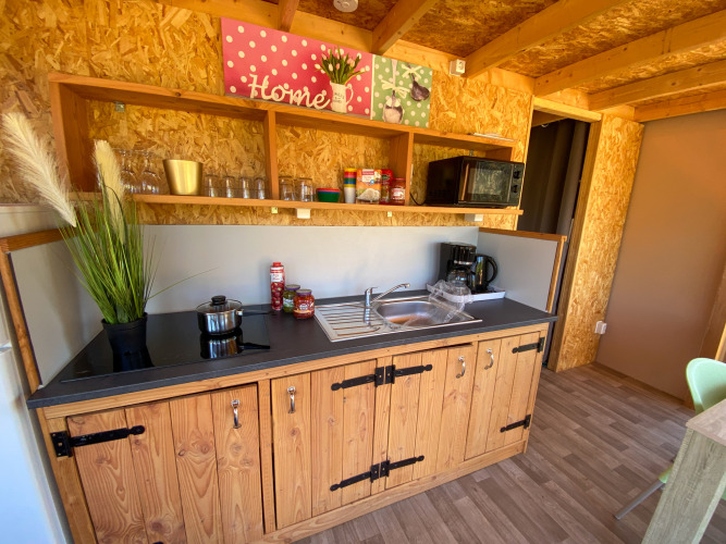 Keukengedeelte in de luxe lodgetent Belle Vue bij La Draille, Frankrijk, met houten kasten en planken.