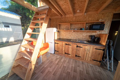 Intérieur d'une tente lodge de luxe à La Draille, France, avec cuisine, escalier en bois et grande fenêtre.