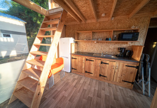 Intérieur d'une tente lodge de luxe à La Draille, France, avec cuisine, escalier en bois et grande fenêtre.