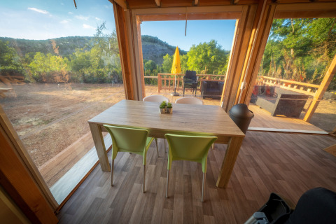 Zona de comedor dentro de la tienda Belle Vue en La Draille, Francia, con vistas a la naturaleza y terraza.