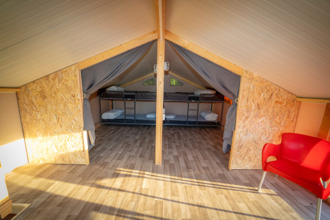 Interieur van de luxe lodge tent Belle Vue op La Draille in Frankrijk met stapelbedden en rode stoel.
