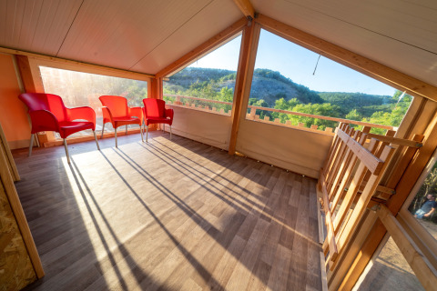 Espacio soleado en tienda safari Belle Vue en La Draille, Francia, con sillas rojas y vistas a la naturaleza.