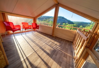 Espacio soleado en tienda safari Belle Vue en La Draille, Francia, con sillas rojas y vistas a la naturaleza.