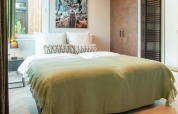 Bedroom at Veluwehoeve Wellness lodge with double bed, green blanket, nature view, and deer wall art.