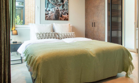 Bedroom at Veluwehoeve Wellness lodge with double bed, green blanket, nature view, and deer wall art.
