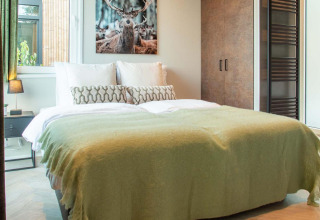 Dormitorio en Veluwehoeve Wellness lodge con cama doble, manta verde y cuadro de ciervo en la pared.