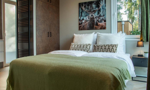 Cozy bedroom at Veluwehoeve Wellness Lodge with a double bed, deer artwork, and sunlight from the window.