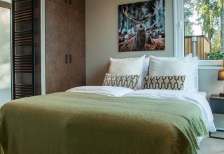 Chambre confortable à la Veluwehoeve Wellness Lodge avec lit double, tableau de cerf et fenêtre ensoleillée.