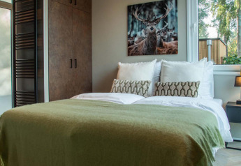 Cozy bedroom at Veluwehoeve Wellness Lodge with a double bed, deer artwork, and sunlight from the window.