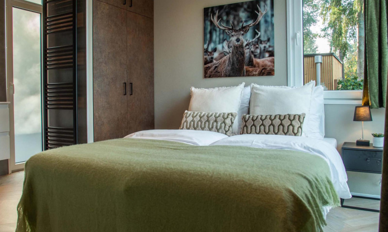 Acogedor dormitorio en Veluwehoeve Wellness Lodge con cama doble, cuadro de ciervo y luz natural exterior.